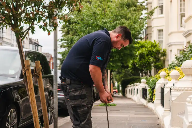 Engineer listening at a street stop tap cover on a pavement of terraced houses