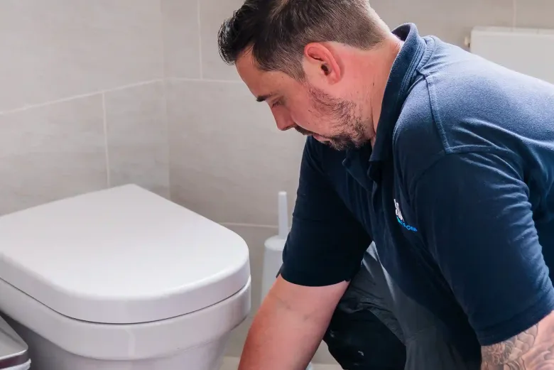 Engineer taking a moisture meter reading on a bathroom floor beside a toilet