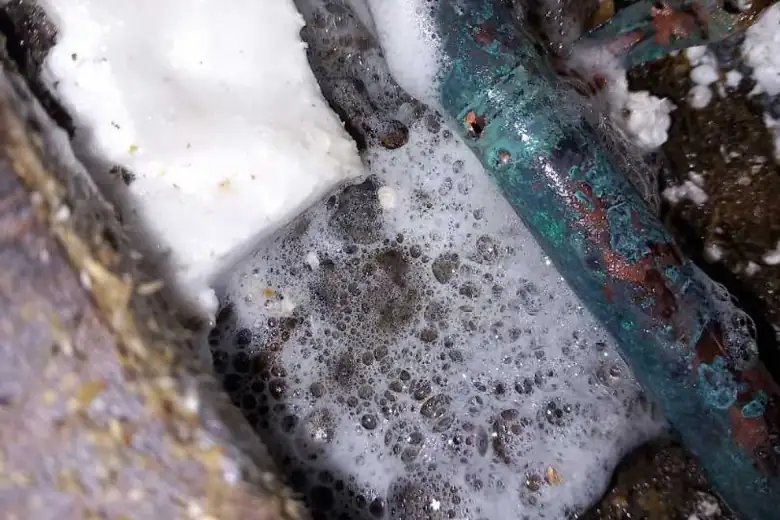 Leak located at heavily corroded copper pipe beneath kitchen floor with water and foam present
