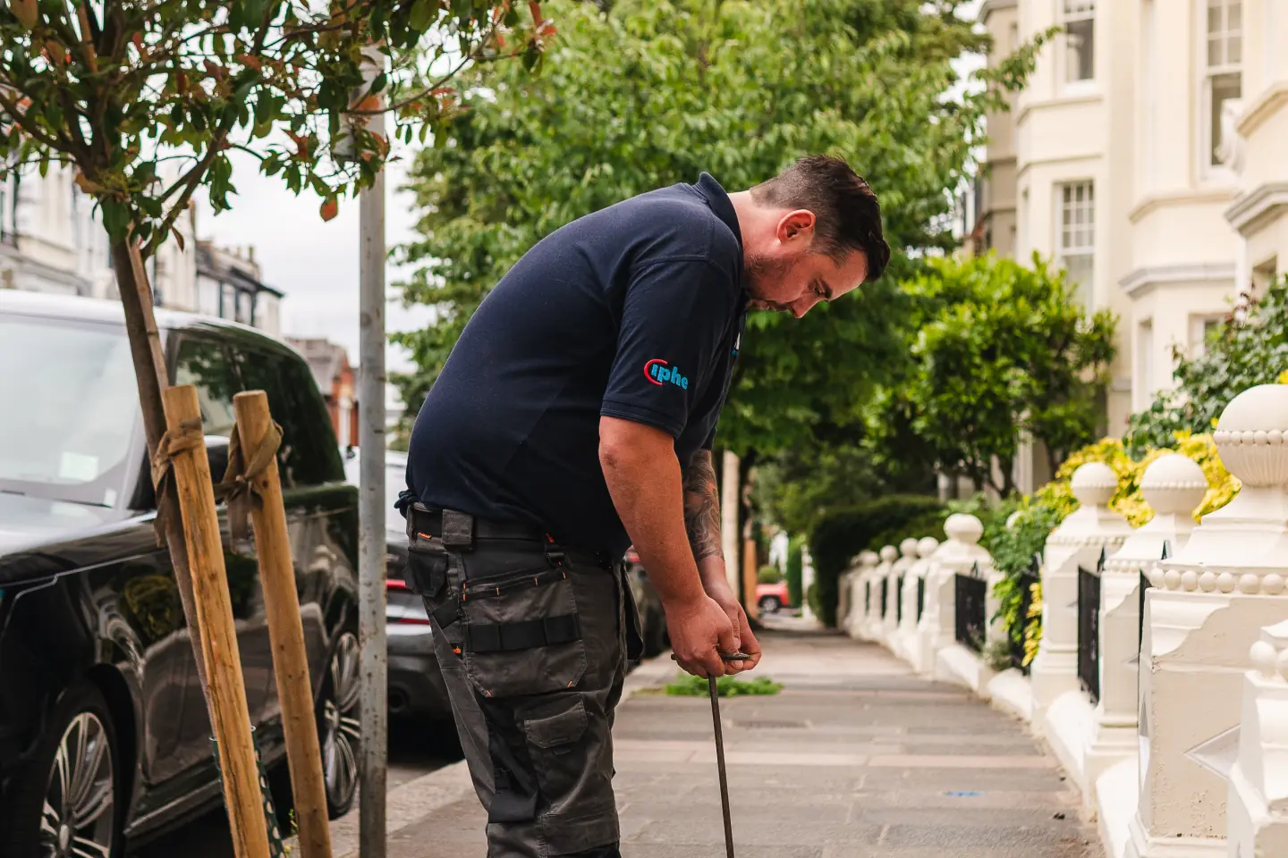 Engineer listening at a street stop tap cover on a pavement of terraced houses